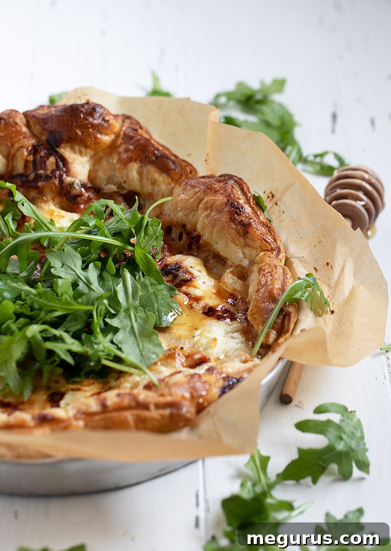 Close-up of a goat cheese tart with arugula and honey, showcasing its golden crust and creamy filling.