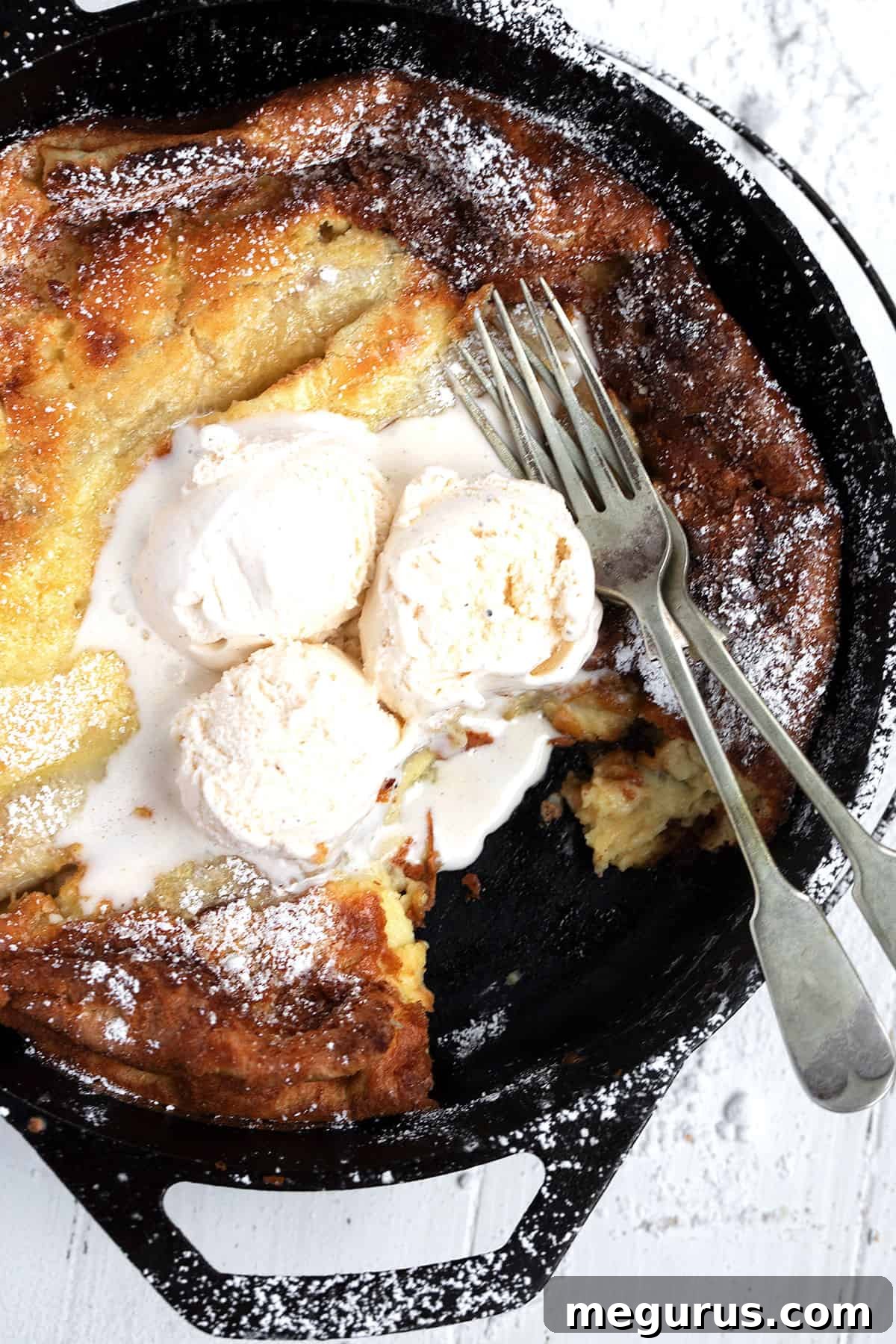 Close-up of the Bananas Foster Dutch Baby, showing its puffed golden edges, caramelized banana slices, and a dollop of melting ice cream.