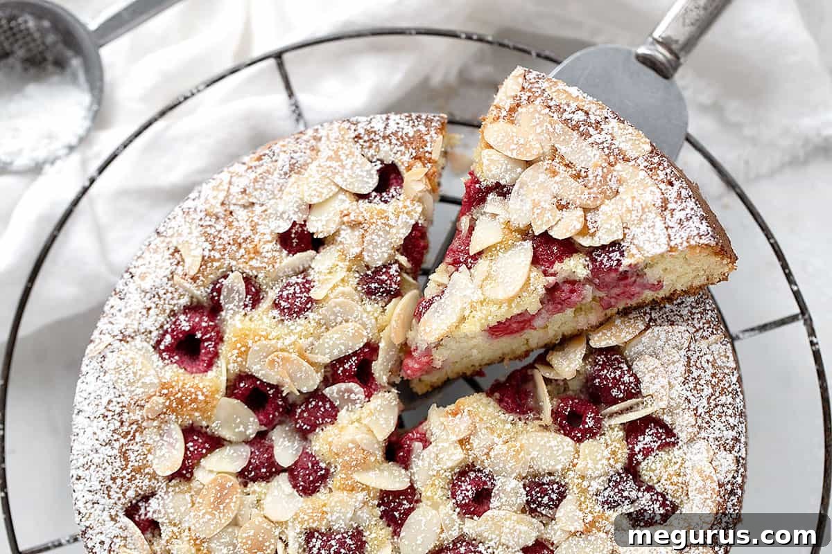 A beautifully sliced raspberry buttermilk cake with a golden crust and vibrant red raspberries, resting on a cooling rack, signifying its readiness for enjoyment.
