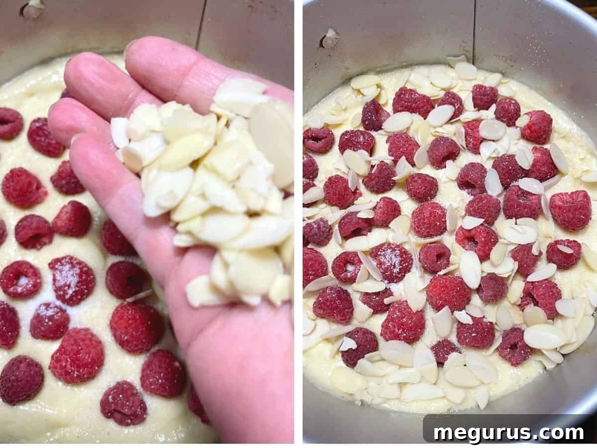 A close-up image of a prepared cake batter in a baking pan, generously topped with fresh raspberries and sprinkled with sugar, ready for the final addition of optional flaked almonds.