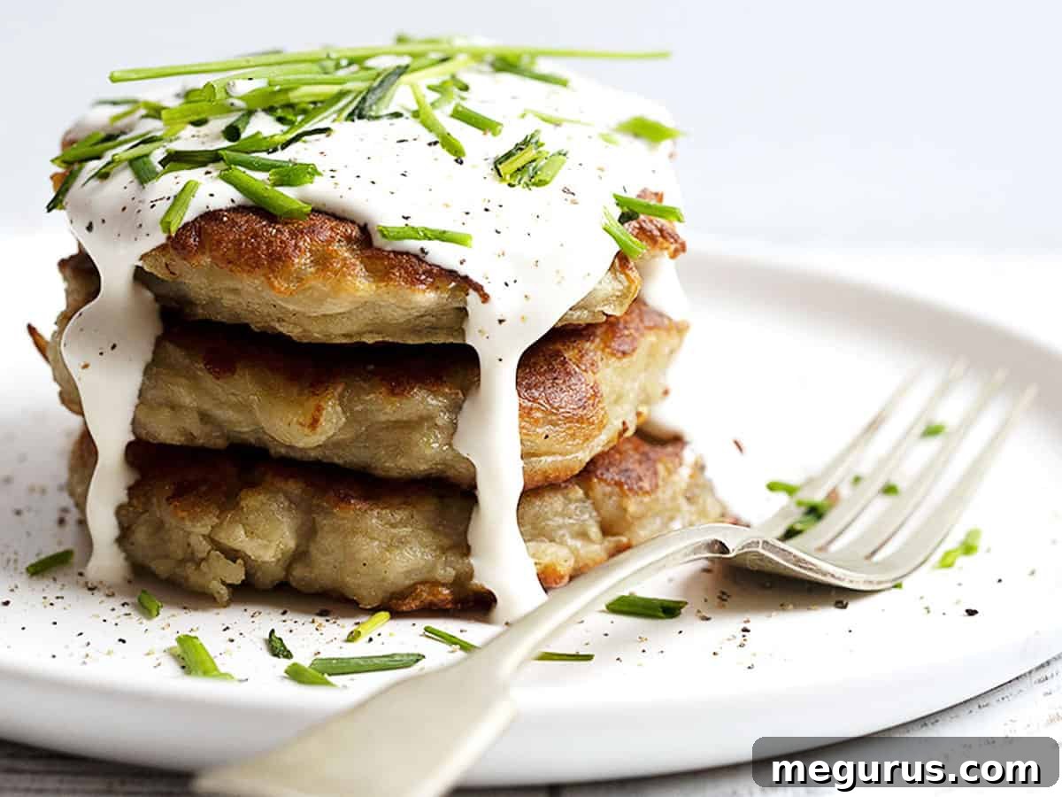 Stacked Irish Boxty potato cakes on a white plate, topped with a dollop of sour cream and fresh green onions, ready to be served as a traditional Irish dish.