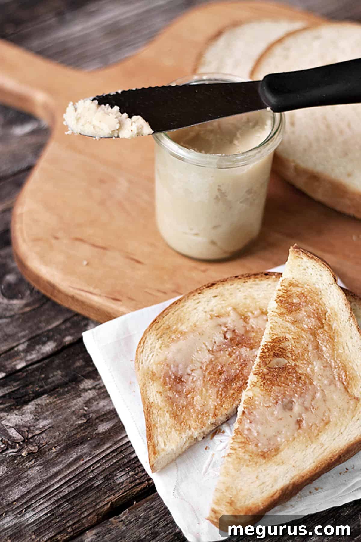 Maple butter in a glass jar next to slices of toast on a wooden cutting board