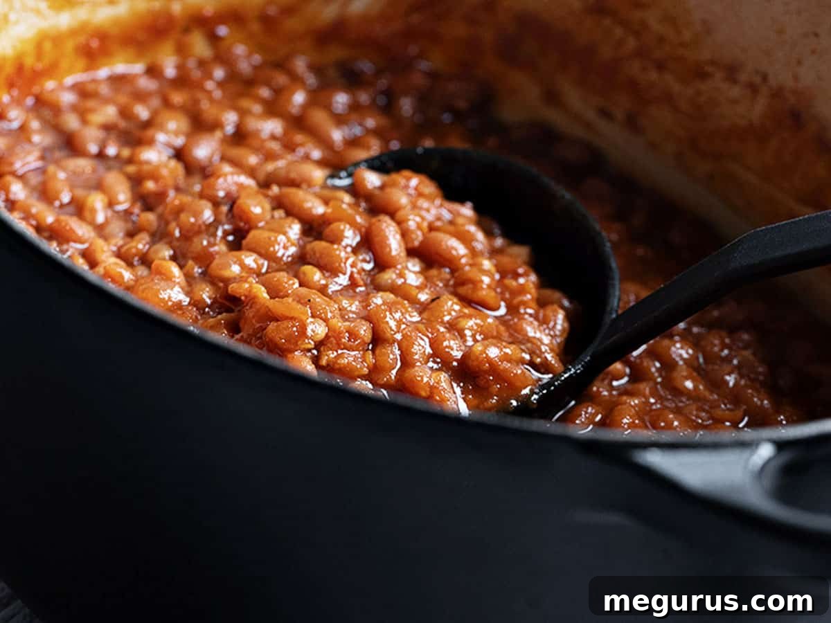 Homemade baked beans in a black casserole dish with a ladle, showcasing a rich, thick sauce and tender beans.