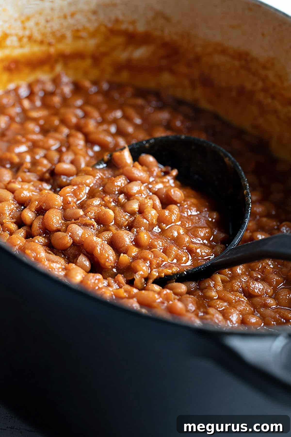 A generous serving of homemade baked beans in a black casserole dish, ready to be enjoyed as a comforting side.