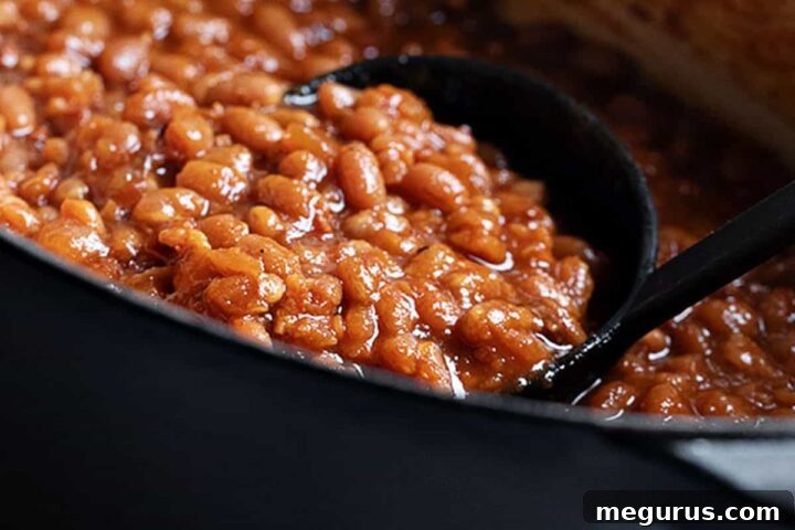 Homemade baked beans in a black casserole with a ladle, showcasing their rustic appeal and rich sauce.