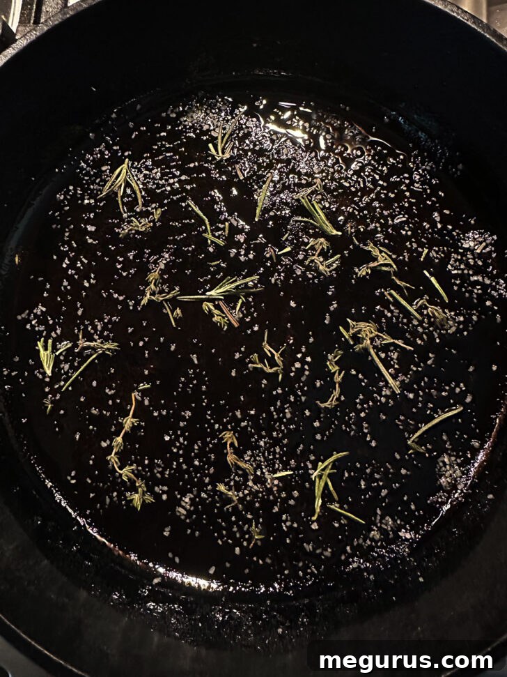 Rosemary and coarse salt scattered on the bottom of a cast iron skillet with olive oil