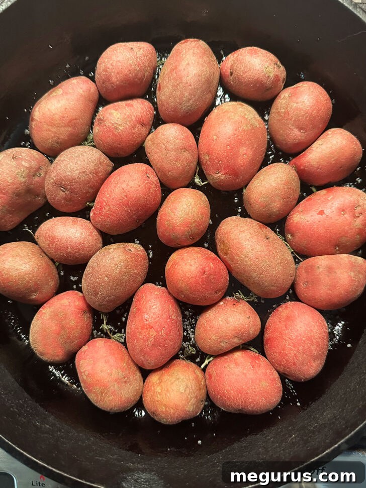 Halved baby potatoes placed cut side down in a single layer in a cast iron skillet