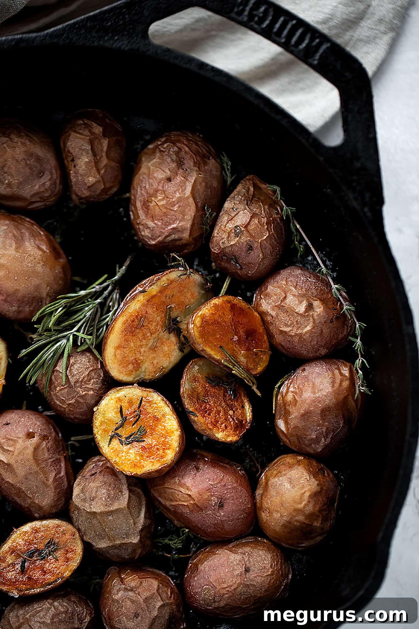 Close-up of golden brown crispy skillet baby potatoes with rosemary in a cast iron pan
