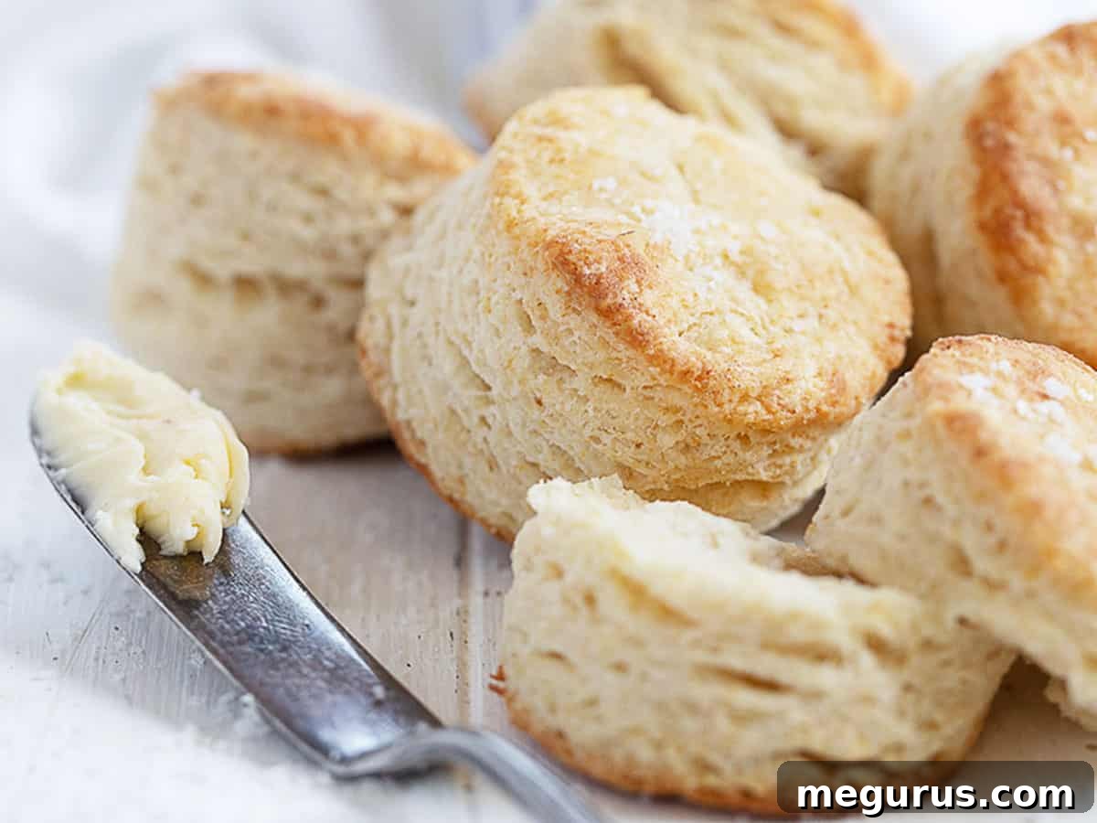 Golden brown, flaky buttermilk biscuits on a wooden board with a knife and butter, ready to be served.