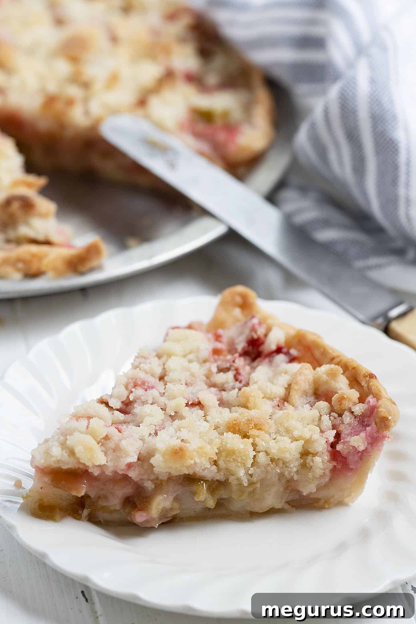 A slice of rhubarb crumble pie on a white plate, showcasing the filling and topping.