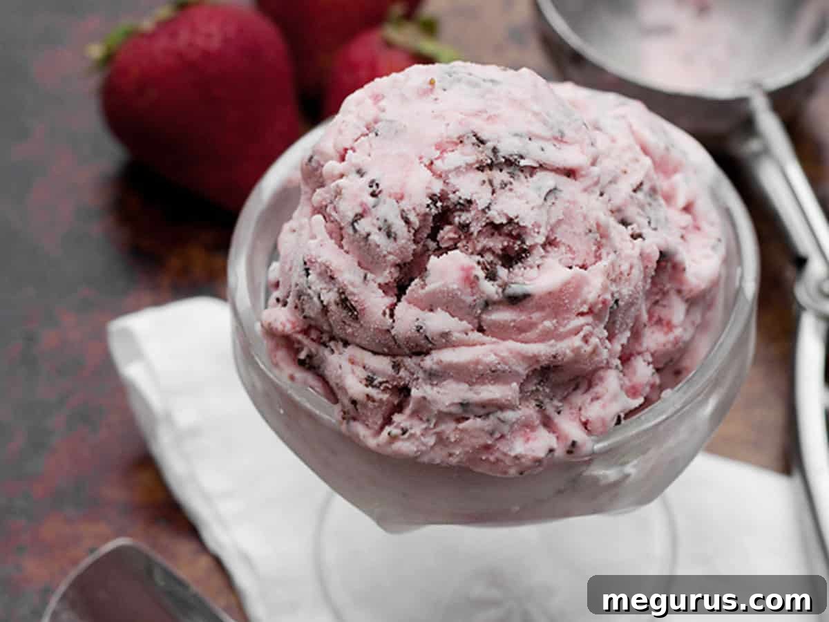 Rich chocolate strawberry ice cream in a clear bowl with a scoop, showcasing its vibrant color and tempting swirl.
