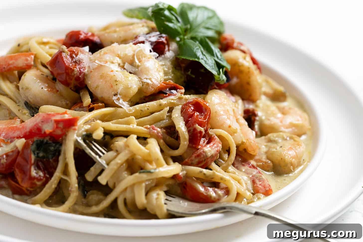 Creamy pasta with shrimp and pesto on a plate with a fork, garnished with fresh basil.