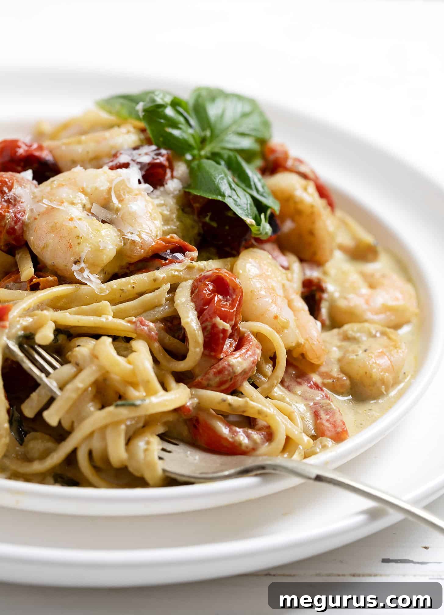 Close-up of creamy shrimp pesto pasta on a white plate with a fork, garnished with fresh basil leaves.