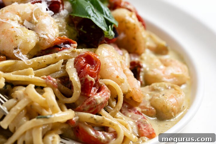 A dish of creamy pasta with shrimp and pesto, garnished with fresh herbs and cheese.