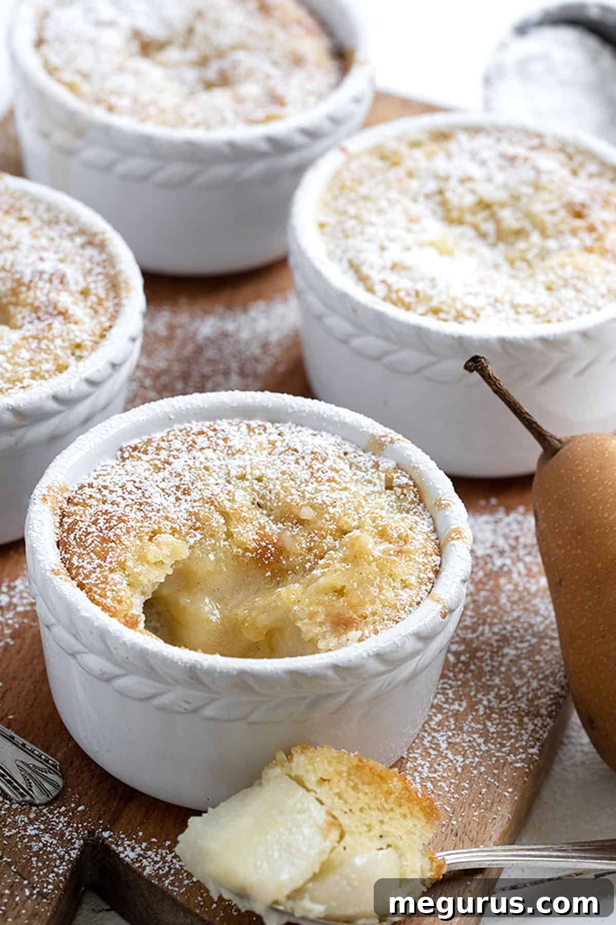 Two individual pear pudding cakes in ramekins, close-up shot showing the topping and baked texture.