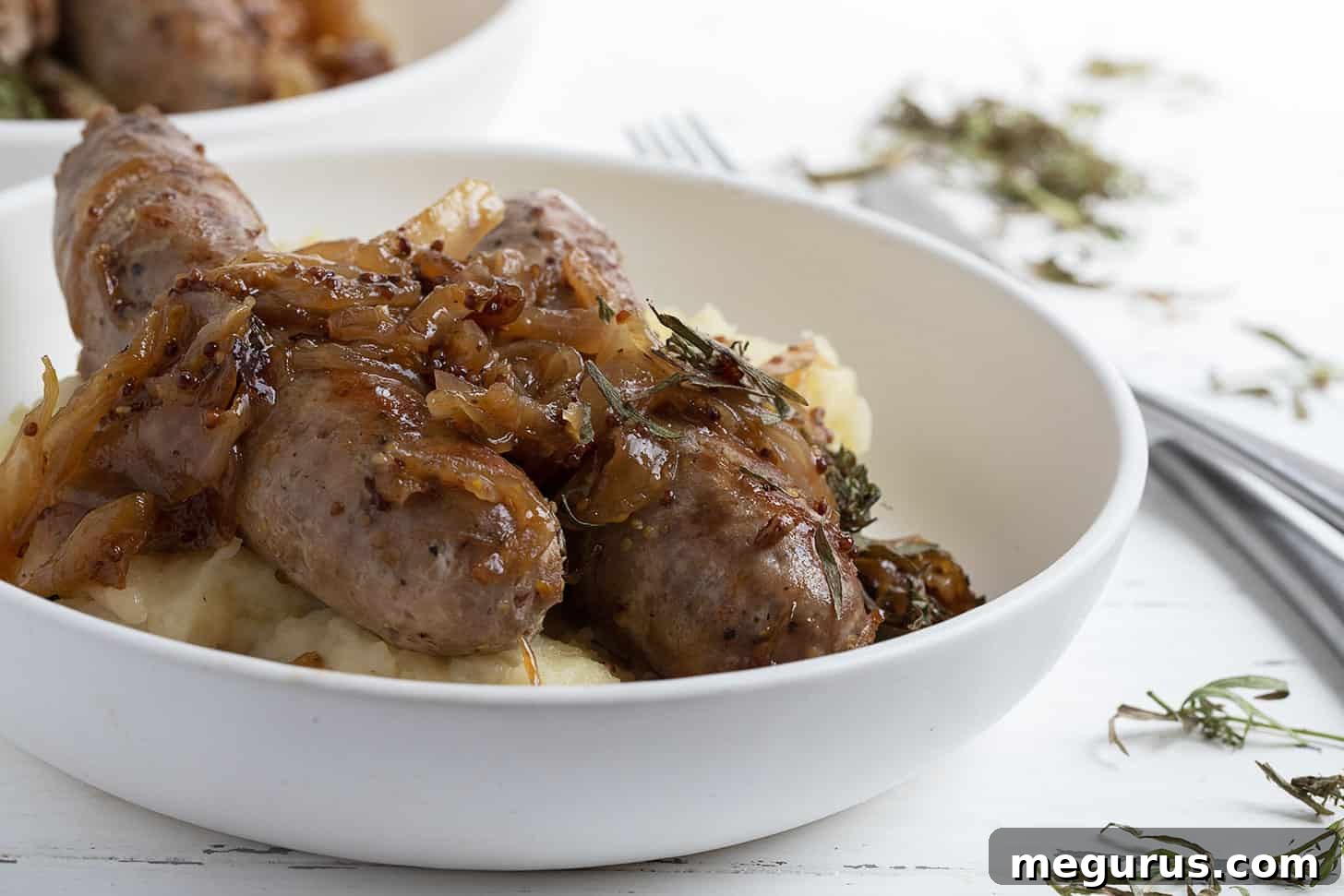 Golden brown pan-fried pork sausage with a generous topping of caramelized mustard onions, served in a rustic bowl.