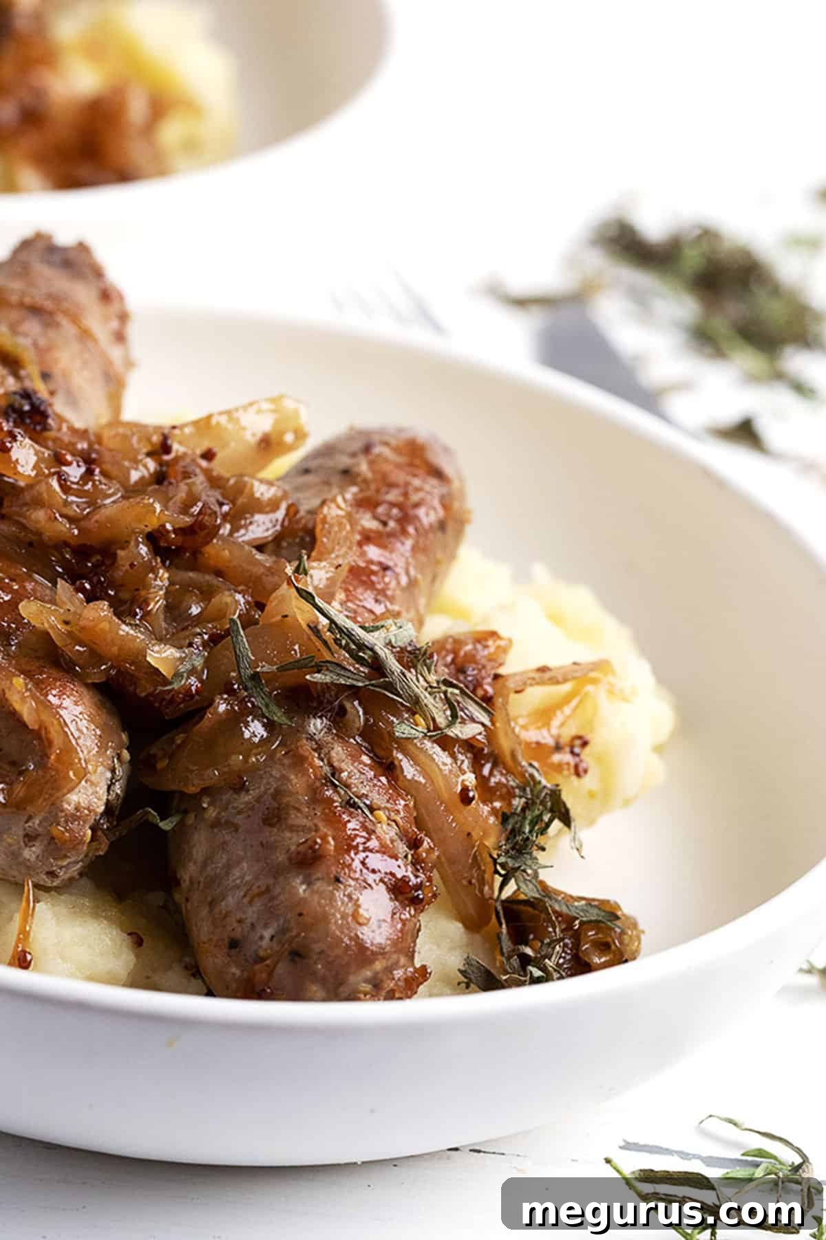 Close-up of a rustic bowl featuring pan-fried pork sausage with caramelized mustard onions, served alongside a creamy potato pear mash.