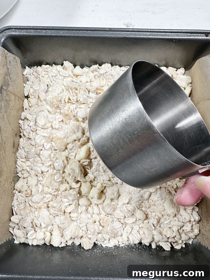 Pressing half of the crumb mixture into the bottom of a parchment-lined baking pan.