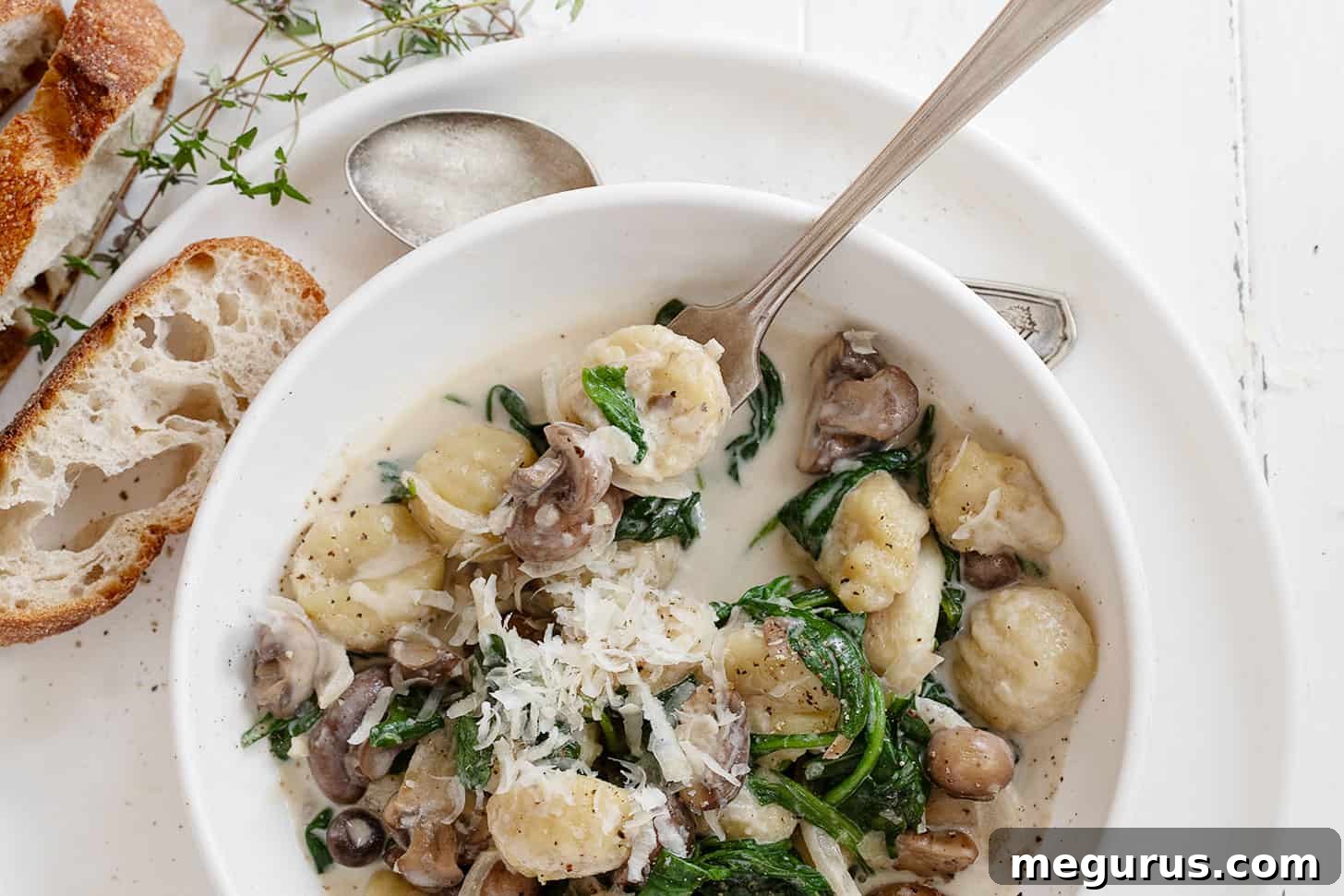 Creamy gnocchi with sautéed mushrooms and fresh spinach in a white bowl, ready to eat with a fork