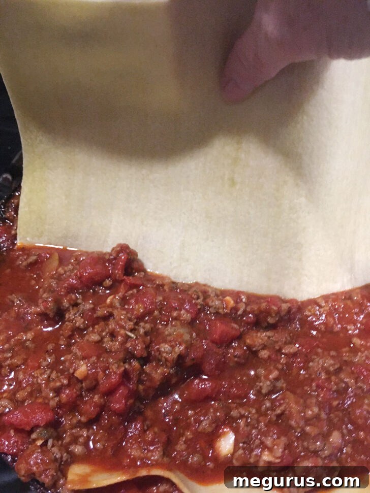 Sliding fresh lasagna noodles carefully into the rich meat sauce.
