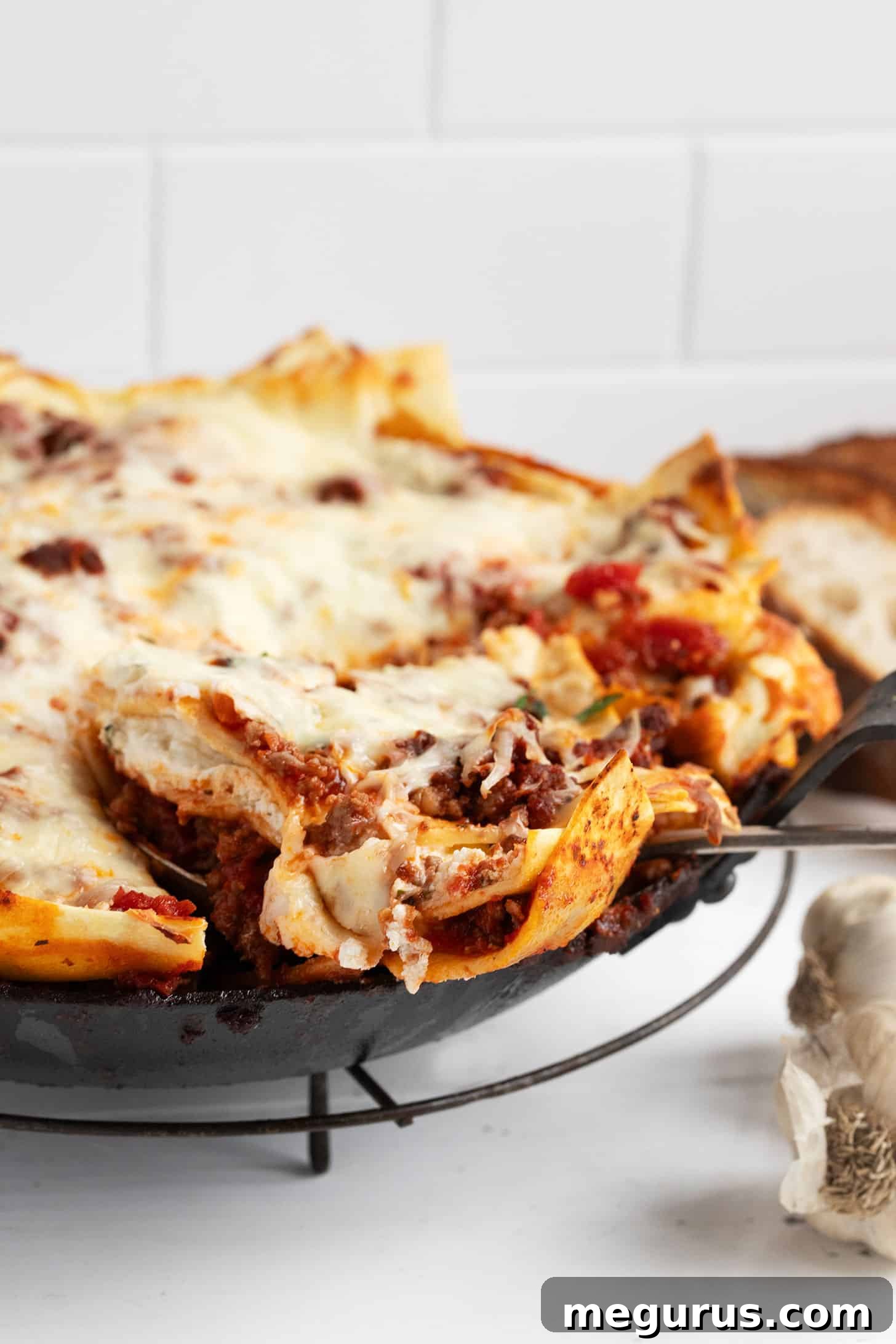 A generous slice of skillet lasagna, revealing layers of pasta, meat sauce, and ricotta cheese.