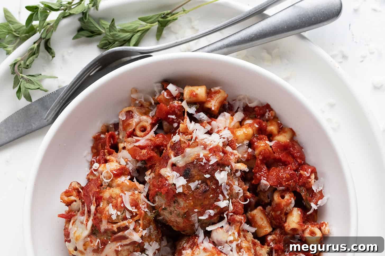 Close-up of a bubbling pork meatball pasta bake in a white bowl, freshly out of the oven.