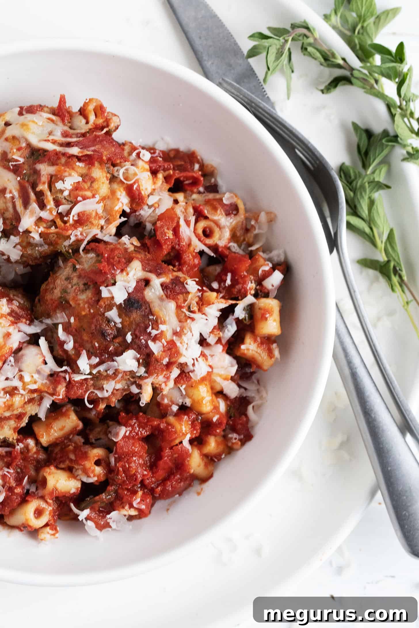 Delicious pork meatball pasta bake served in a white bowl, garnished with fresh herbs.