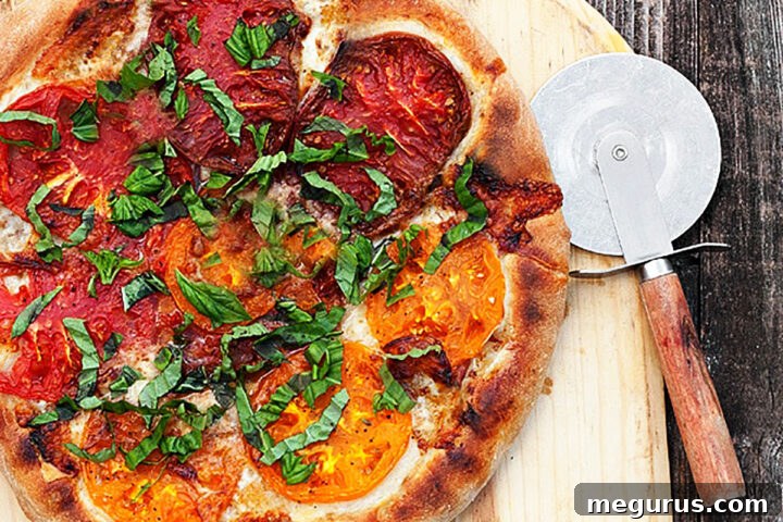 A vibrant whole heirloom tomato pizza, freshly baked and placed on a pizza peel with a pizza cutter nearby