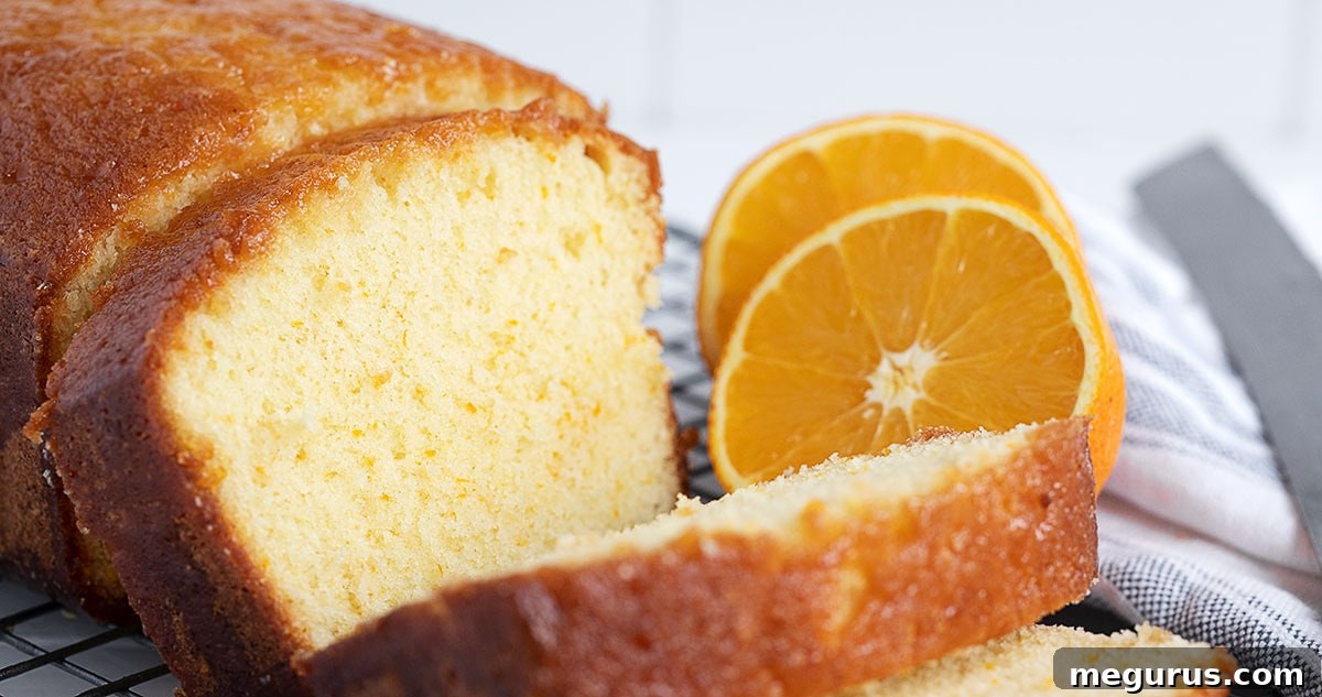 Sliced orange drizzle loaf cake with halved oranges on a wooden board.