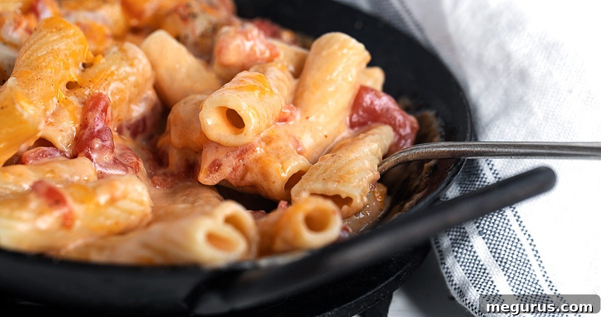 A large bowl of creamy pasta with cheese and diced tomatoes, ready to be served