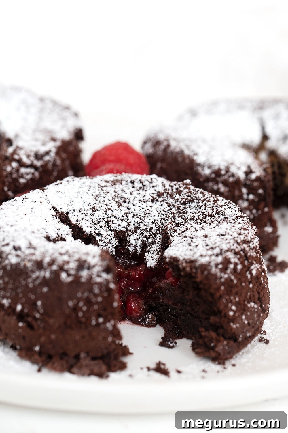 A single, perfectly baked chocolate molten cake with a luscious raspberry filling, elegantly placed on a white plate alongside a fork, inviting a delightful indulgence.
