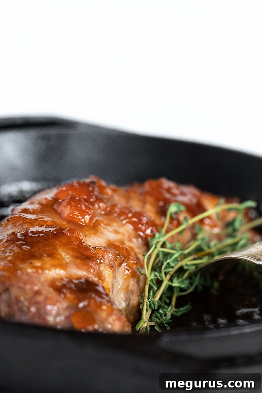 Close-up of sliced apricot mustard glazed pork tenderloin in a cast iron skillet, garnished and ready to be served.