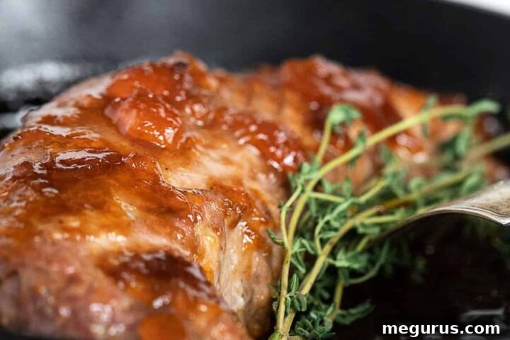 Close-up of delicious apricot mustard pork tenderloin in a cast iron skillet, sliced and garnished.