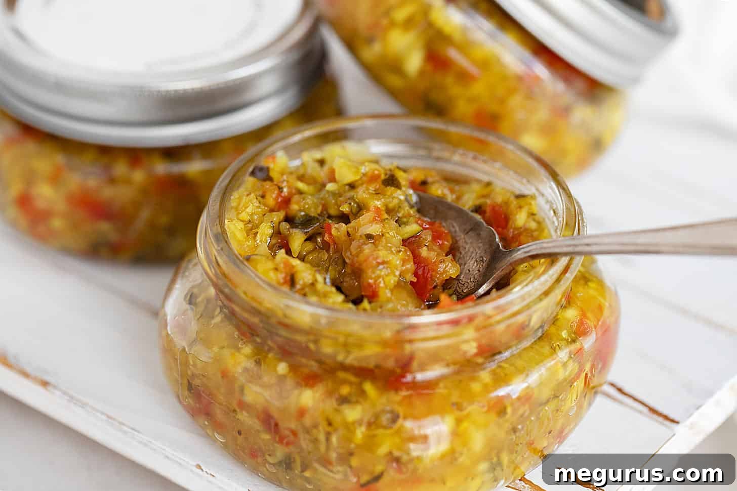 Beautiful jars of homemade zucchini mustard relish with a serving spoon.
