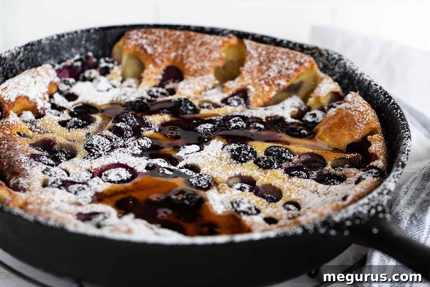 Golden blueberry Dutch baby with savory sausage links in a cast iron skillet, ready to serve for breakfast or brunch.