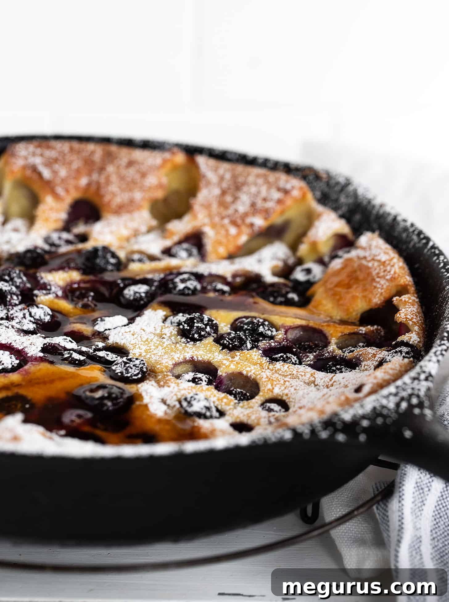 Close-up of a blueberry Dutch baby with sausage in a cast iron skillet, golden brown and puffed up, ready to be served.
