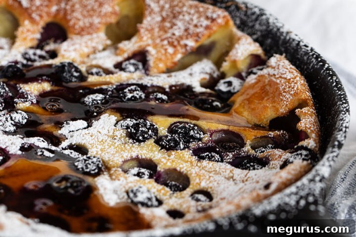 Delicious blueberry Dutch baby with sausage in a cast iron skillet, ready to serve as a hearty breakfast.