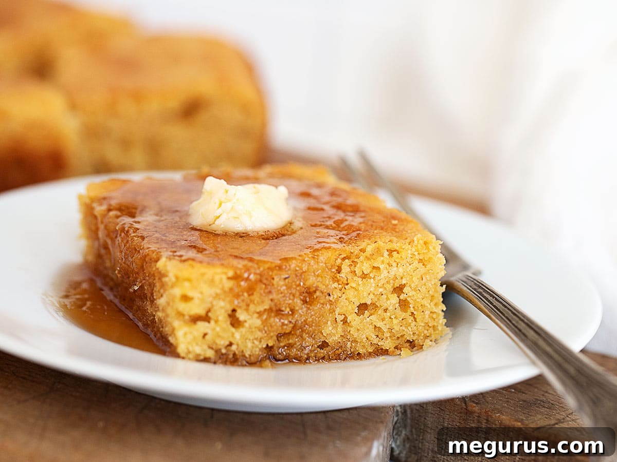 Golden Johnny Cake squares drizzled generously with amber maple syrup and melting butter, ready to be served on a rustic plate.