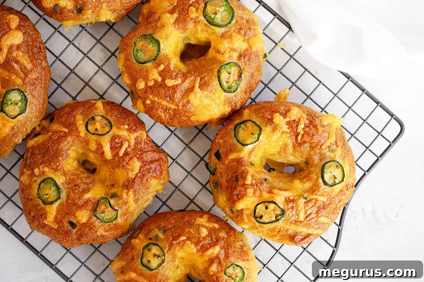 Freshly baked jalapeño cheddar bagels cooling on a wire rack, showing golden brown crust and melted cheese