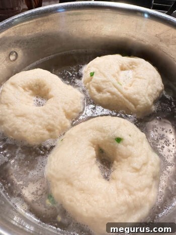 Bagels being carefully boiled in a large pot of water on the stove