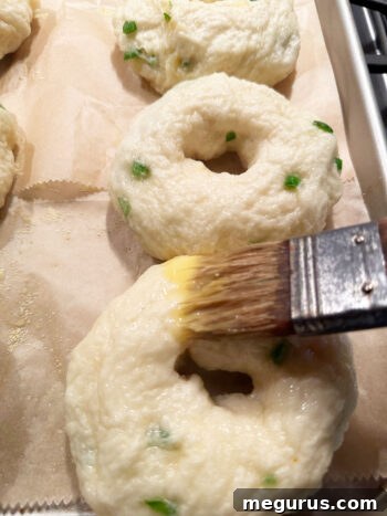 Brushing boiled bagels with an egg wash for a golden, shiny finish