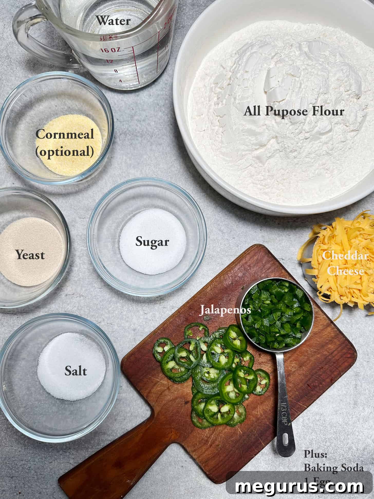 Various ingredients laid out on a wooden board for making jalapeño cheddar bagels, including flour, cheese, and fresh jalapeños