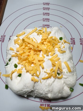 Kneading diced jalapeño and shredded cheddar into bagel dough on a floured surface