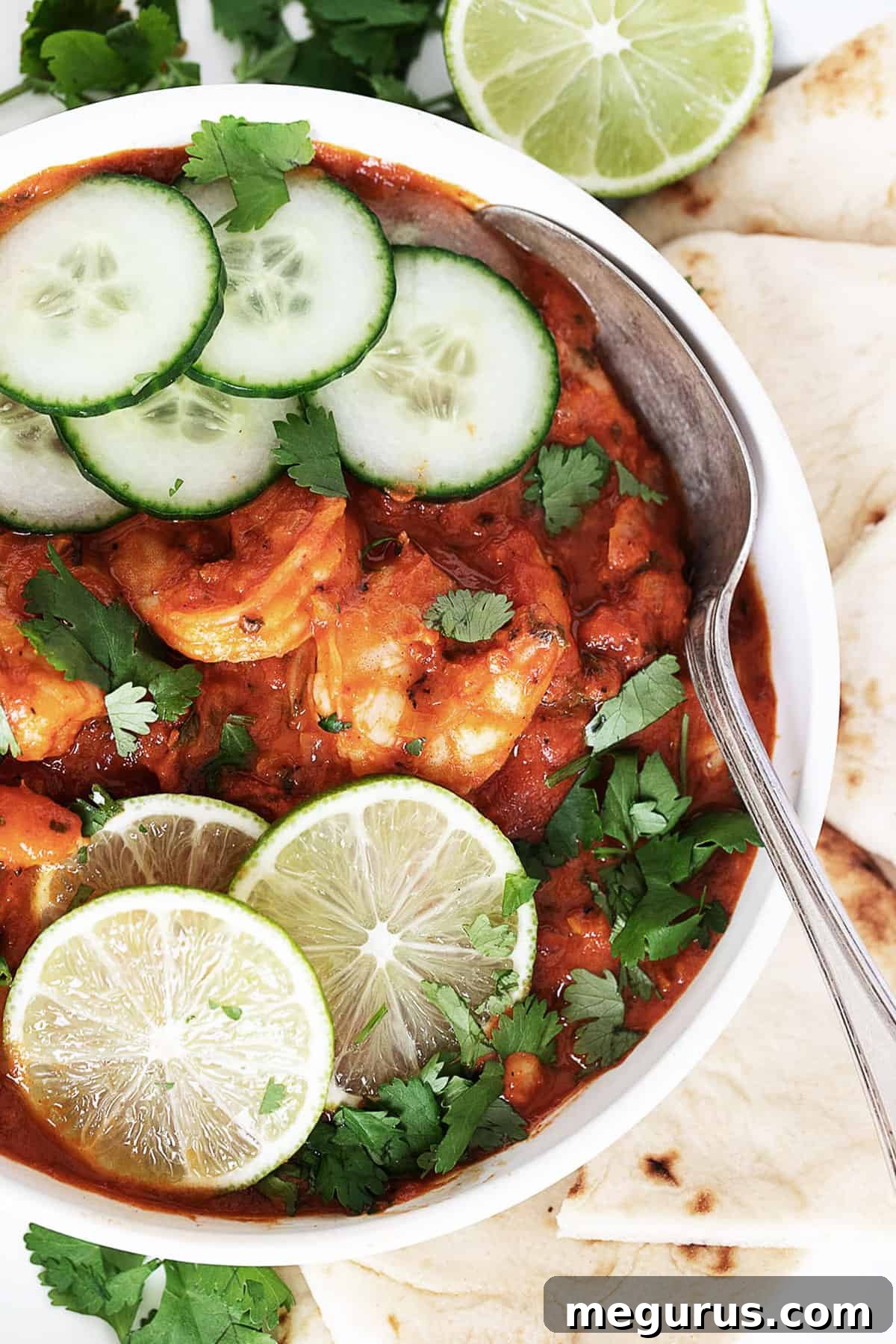 A vibrant bowl of Indian Butter Shrimp, garnished with fresh cilantro, a slice of lime, and cucumber, showcasing its rich texture.