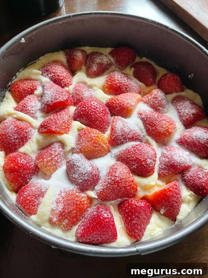 Strawberry yogurt cake batter topped with halved strawberries and a sprinkle of sugar