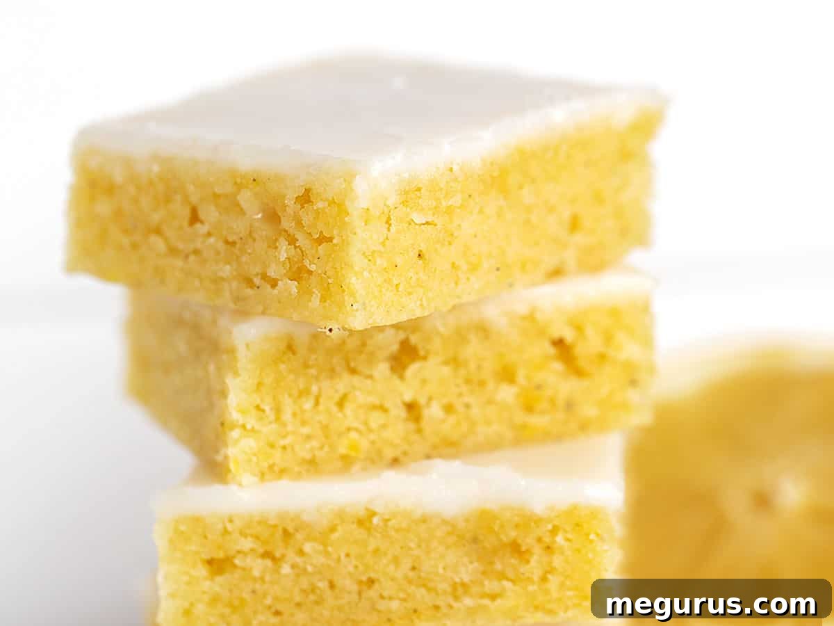 Stacked lemon blondies with a fresh lemon slice behind them, highlighting their vibrant citrus appeal