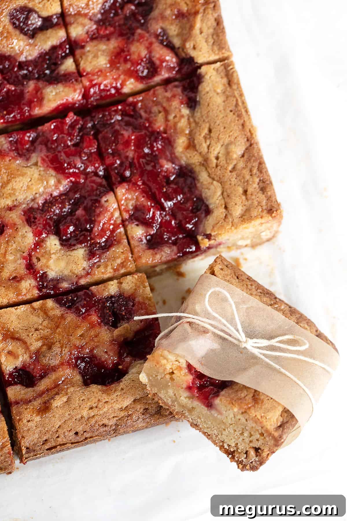 Individual strawberry blondies wrapped in parchment paper and tied with string, ideal for a picnic.