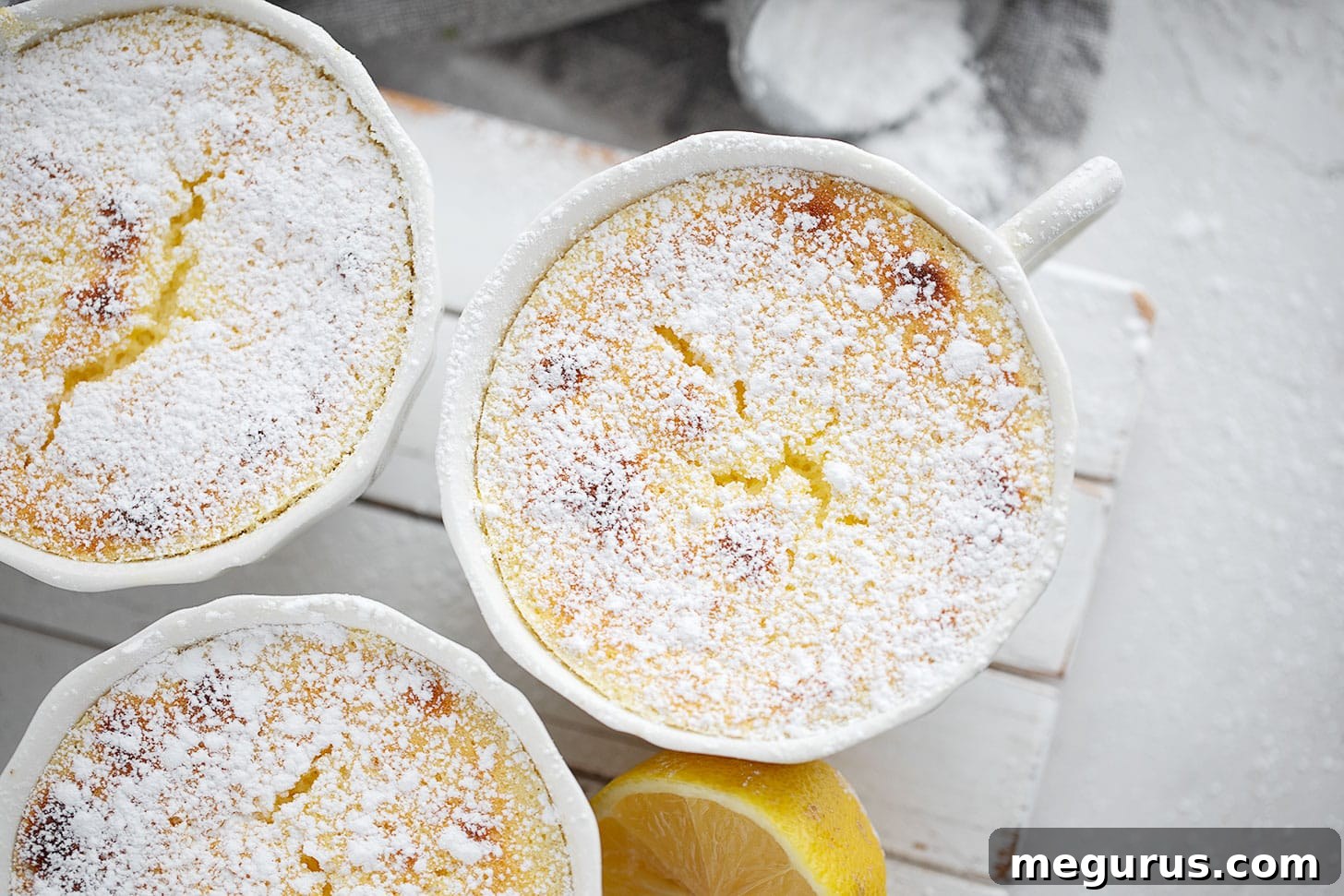 Six golden-brown lemon pudding cakes elegantly arranged on a white serving stand, garnished with a light dusting of powdered sugar and fresh lemon slices.