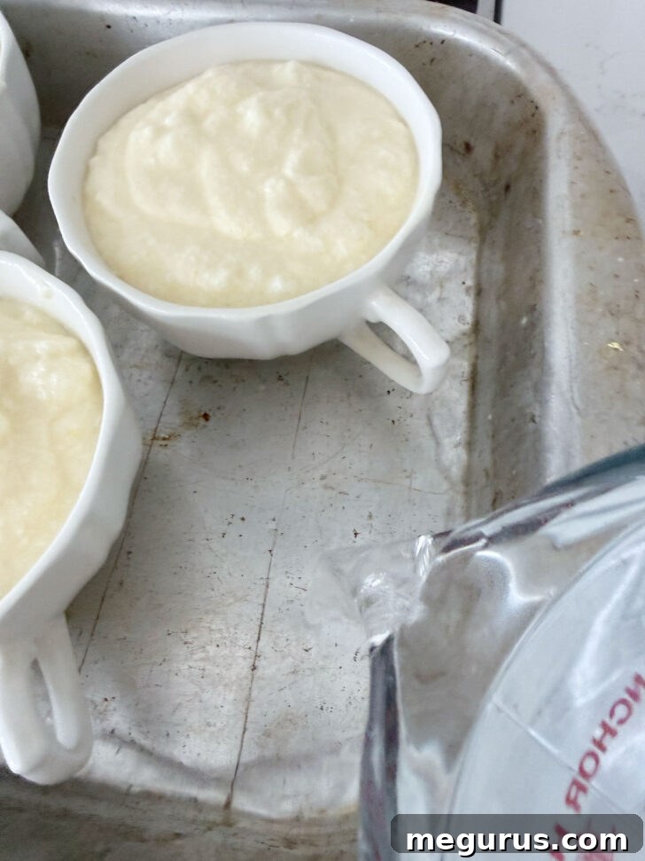Lemon pudding cake batter neatly spooned into individual oven-safe ramekins, placed within a roasting pan filled halfway with hot water for a water bath.