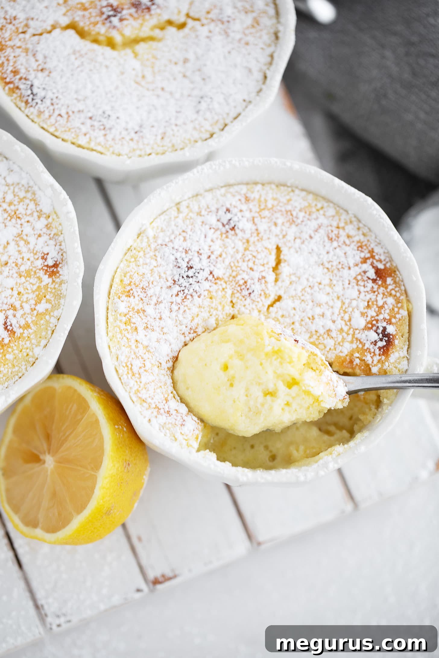 A close-up of a finished lemon pudding cake, showing the distinct layers of creamy pudding at the bottom and the light, soufflé-like cake on top, dusted with powdered sugar.